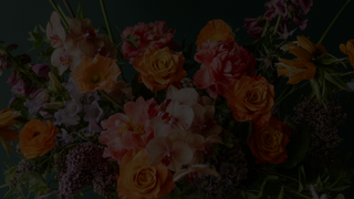 Vibrant floral arrangement featuring roses, orchids, and assorted blossoms in shades of orange and purple.